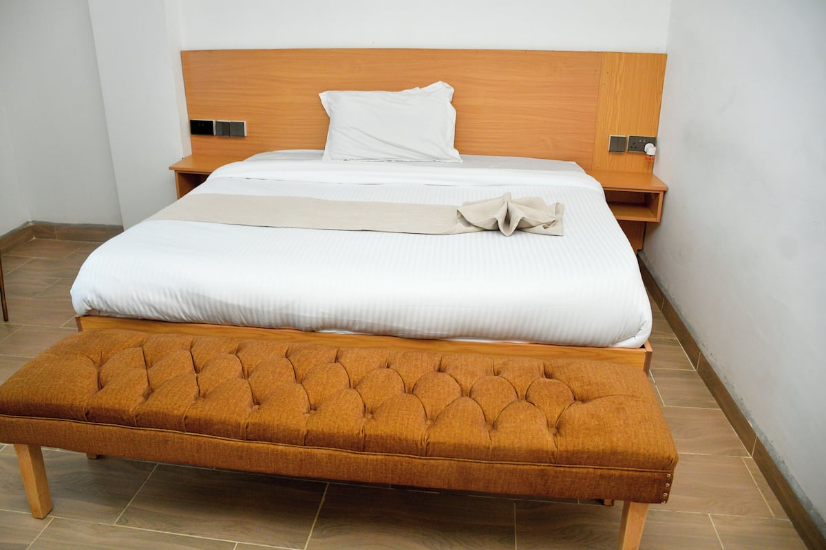 A neatly made bed with a wooden headboard, a bedside table with a lamp, and a bench at the foot of the bed.