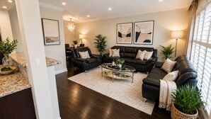 A living room with dark wood flooring, a black leather sofa, a glass coffee table, and two framed abstract paintings on the wall. - Spacious 3BR Toronto Home Near Downtown (Toronto)
