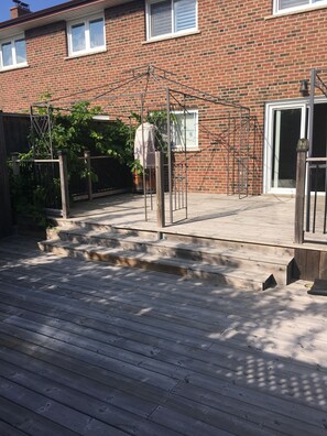 Une terrasse en bois avec une porte en métal, une maison en briques et un pot de fleurs.