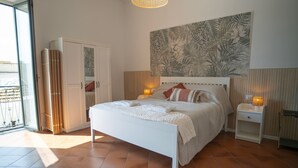 A bedroom with a bed, nightstands, a wall-mounted lamp, a sliding door, and a large floral wall art piece. - Modern Suite and Open Space Bedroom• 200 meters from Sea • into Historic Center (Salerno)