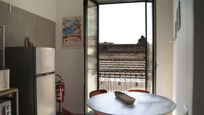 A kitchen with a refrigerator, a table with chairs, a fire extinguisher, and a view through a glass door. - Modern Suite and Open Space Bedroom• 200 meters from Sea • into Historic Center (Salerno)