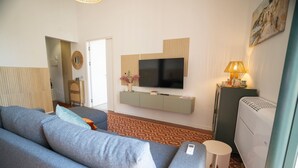 A modern living room with a grey sofa, a flat-screen TV, a small side table with a lamp, and a radiator. - Modern Suite and Open Space Bedroom• 200 meters from Sea • into Historic Center (Salerno)