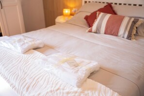 A neatly made bed with a white comforter and pillows, a bedside table with a lamp, and a striped pillow on the headboard. - Modern Suite and Open Space Bedroom• 200 meters from Sea • into Historic Center (Salerno)