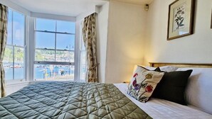 Ein Hotelzimmer mit Bett, einem Fenster mit Vorhängen und einem gerahmten Bild an der Wand.