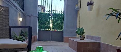 A table with a glass jar, a spoon, and a cup, set against a wall with a gate and potted plants.