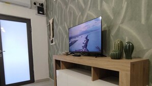 A modern living room with a flat-screen TV on a wooden stand, a white cabinet below, and a patterned wall. - Comfortable house with 2 rooms and full kitchen ideal for families and groups of friends (Napoli)