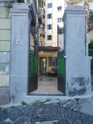 Ingresso di un edificio con un cartello con il numero '43', un cancello e una piccola area esterna con posti a sedere.