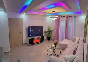 A modern living room with a flat-screen TV, a sofa, a coffee table, and a potted plant. - Welcome to Your Home 15 Minutes From the Airport (Santo Domingo Este)