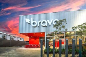 A modern building with a prominent 'bravo' sign, large windows, and a red seating area outside. - Welcome to Your Home 15 Minutes From the Airport (Santo Domingo Este)