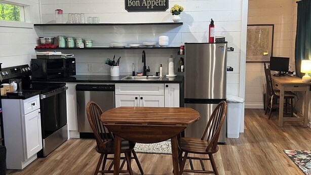 A modern kitchen with white cabinetry, a dining table with chairs, a refrigerator, and an air conditioning unit.