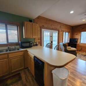 A kitchen with wooden cabinets, a dishwasher, a microwave, and a dining area with chairs. - Huckleberry Cabin-Private (Sevierville)