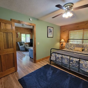 A room with a bed, a blue rug, a ceiling fan, and a window with blinds. - Huckleberry Cabin-Private (Sevierville)