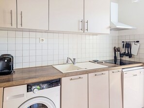 A kitchen with white cabinets, a dishwasher, a washing machine, a sink, and a coffee maker. - Nautica by Interhome (Fréjus)