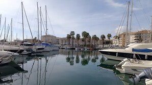 En lystbådehavn med flere både i havnen, en bygning med balkoner og palmer i baggrunden.
