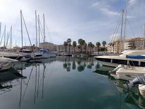 A marina with multiple boats docked, a building with balconies, and palm trees in the background. - Nautica by Interhome (Fréjus)