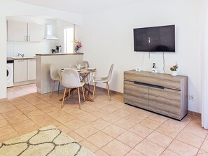 A modern kitchen with white cabinets, a dining area with a round table and chairs, a TV mounted on the wall, and a wooden dresser. - Nautica by Interhome (Fréjus)