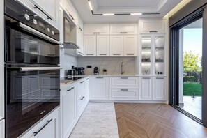 A modern kitchen with white cabinetry, a built-in oven, and a large window. - Luxurious Villa Arthur in Corfu | Heated Pool & Jacuzzi, Sea Views, Outdoor BBQ (Kassiopi)