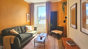 Een gezellige woonkamer met een bank, salontafel en uitzicht door een raam.