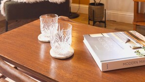 Een kamer met een bed, een nachtkastje met twee glazen en een boek, een vloerlamp en een kamerplant.