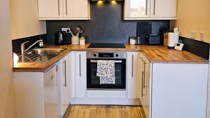 Een kleine keuken met witte kastjes, een inbouwoven, een rvs afzuigkap en een houten aanrecht.