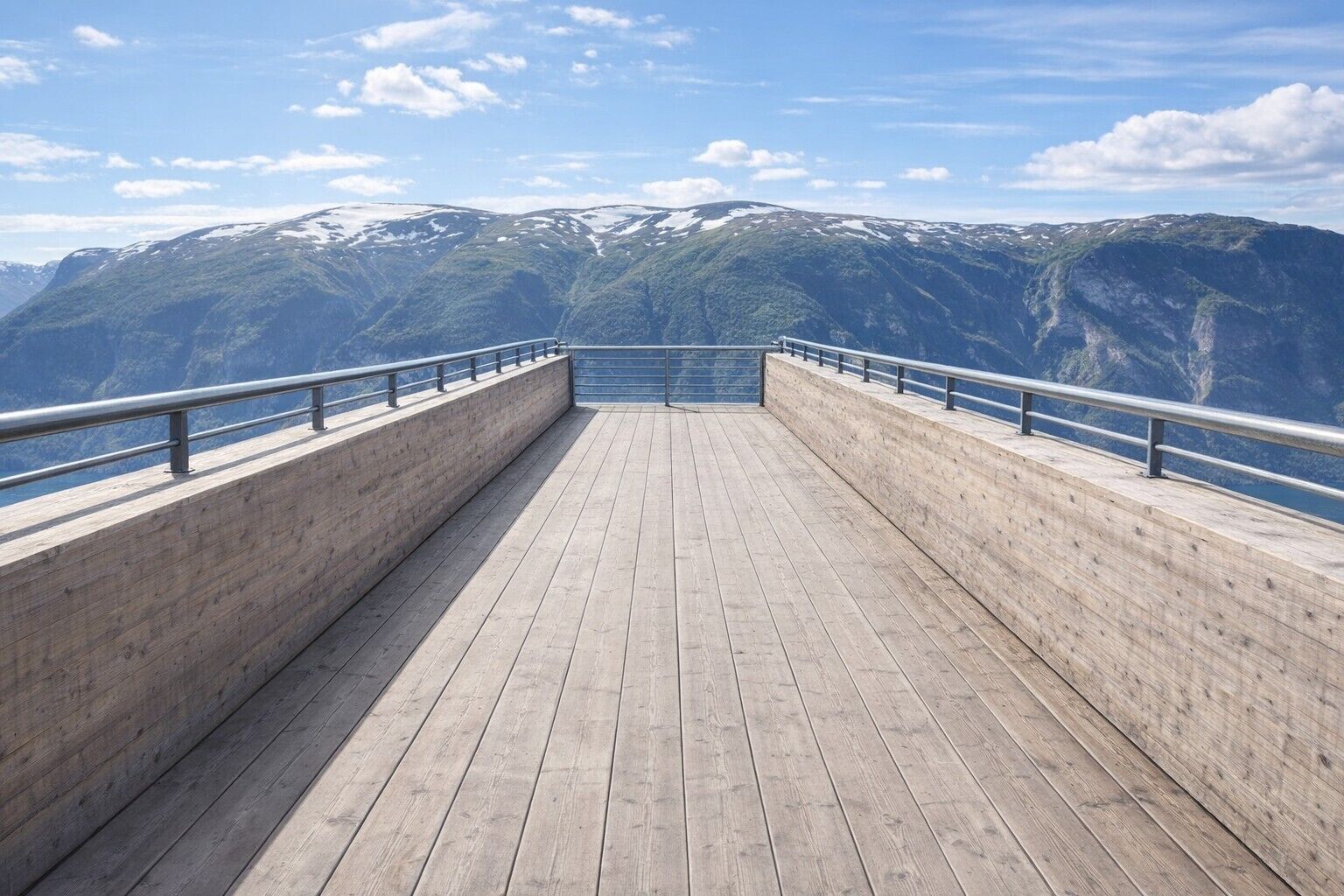 A wooden deck with metal railings, overlooking a mountainous landscape.