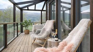 A wooden deck with two lounge chairs, a table with a bottle of champagne, and a potted plant.