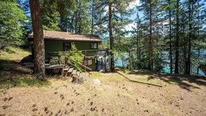 Uma cabana com varanda, escadas e vista para um lago rodeado de árvores.