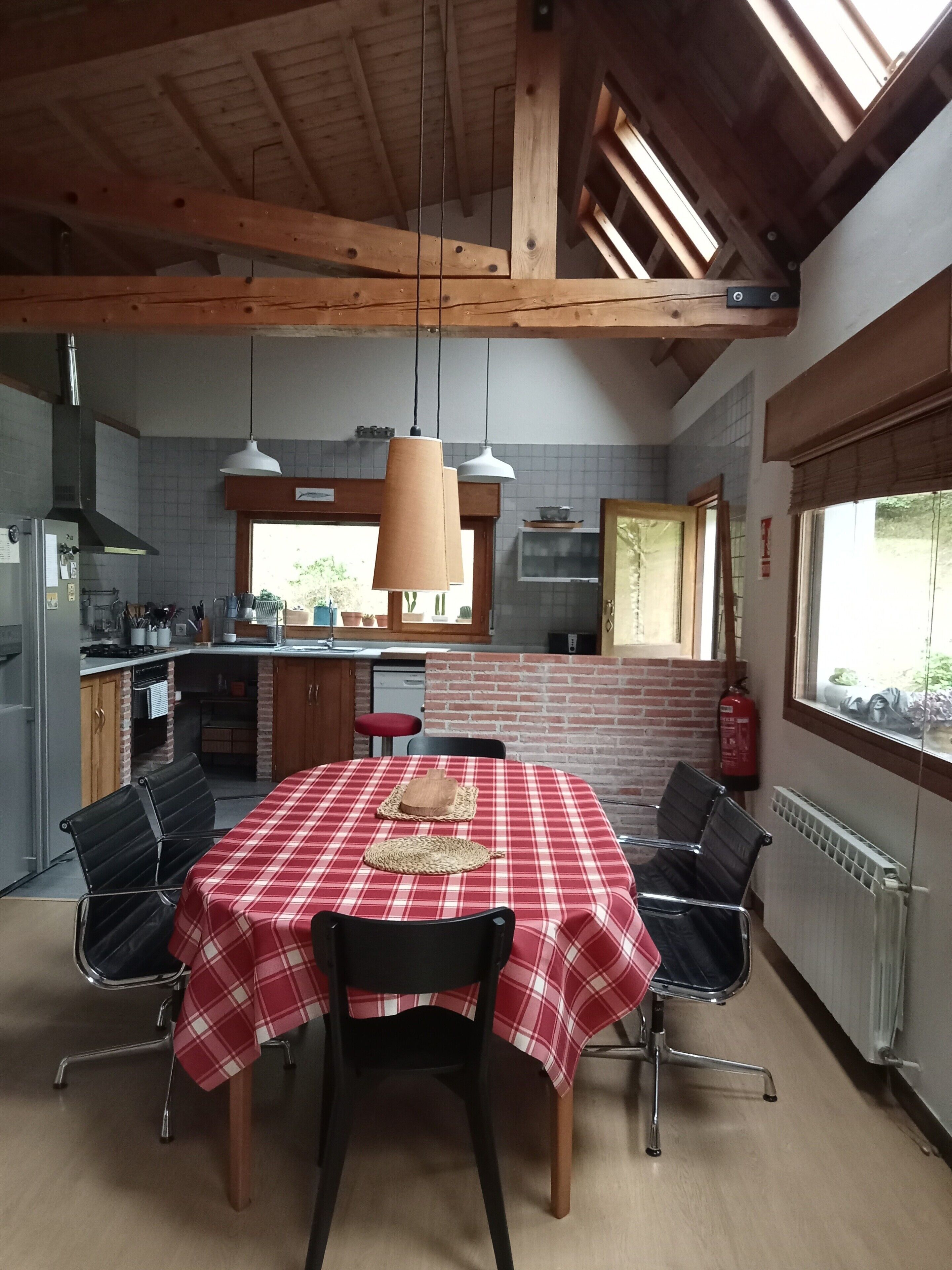 Een keuken met een eethoek, houten balken in het plafond en een rood-wit geruit tafelkleed.