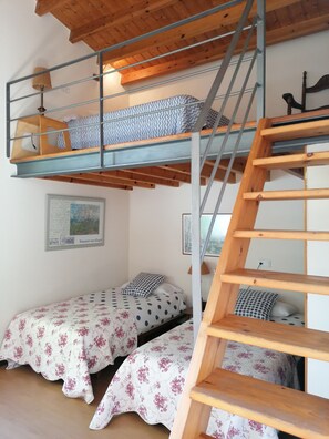 A dormitory room with bunk beds, a wooden ladder, a framed picture on the wall, and a floral bedspread.