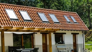 Un bâtiment doté d’un toit recouvert de tuiles, de nombreuses fenêtres, d’un patio abrité avec une table et des chaises, et d’un petit espace extérieur aménagé pour s’asseoir.