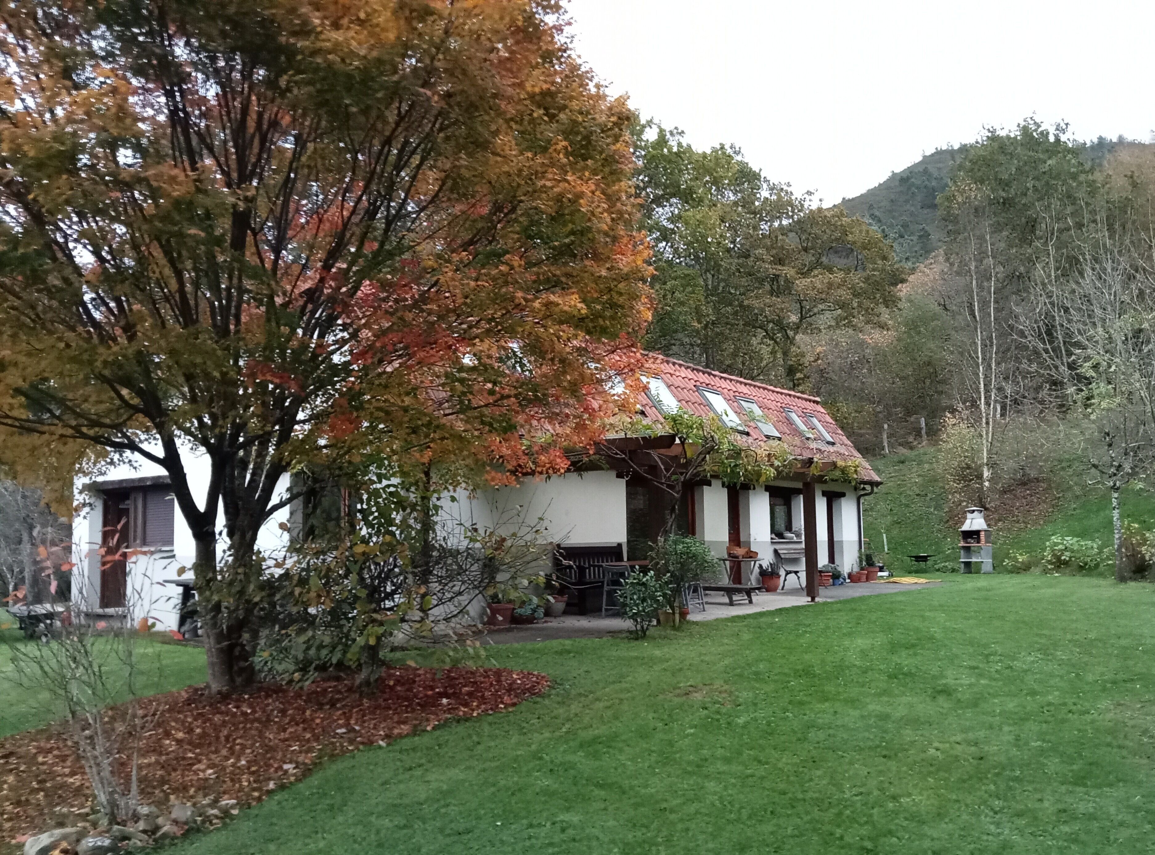 A house with a red-tiled roof, a white exterior, and a garden with a lawn and trees.