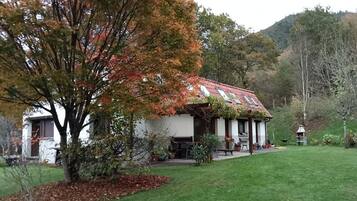 Una casa con tetto in tegole rosse, facciata bianca e un giardino con prato e alberi.