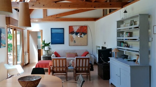 Un vaste espace de vie doté d’un plafond haut, de poutres apparentes, d’une table à manger avec des chaises, d’un canapé et d’un téléviseur.