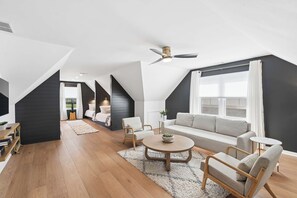 A modern loft with a high ceiling, a ceiling fan, a sofa, a coffee table, and a bookshelf.