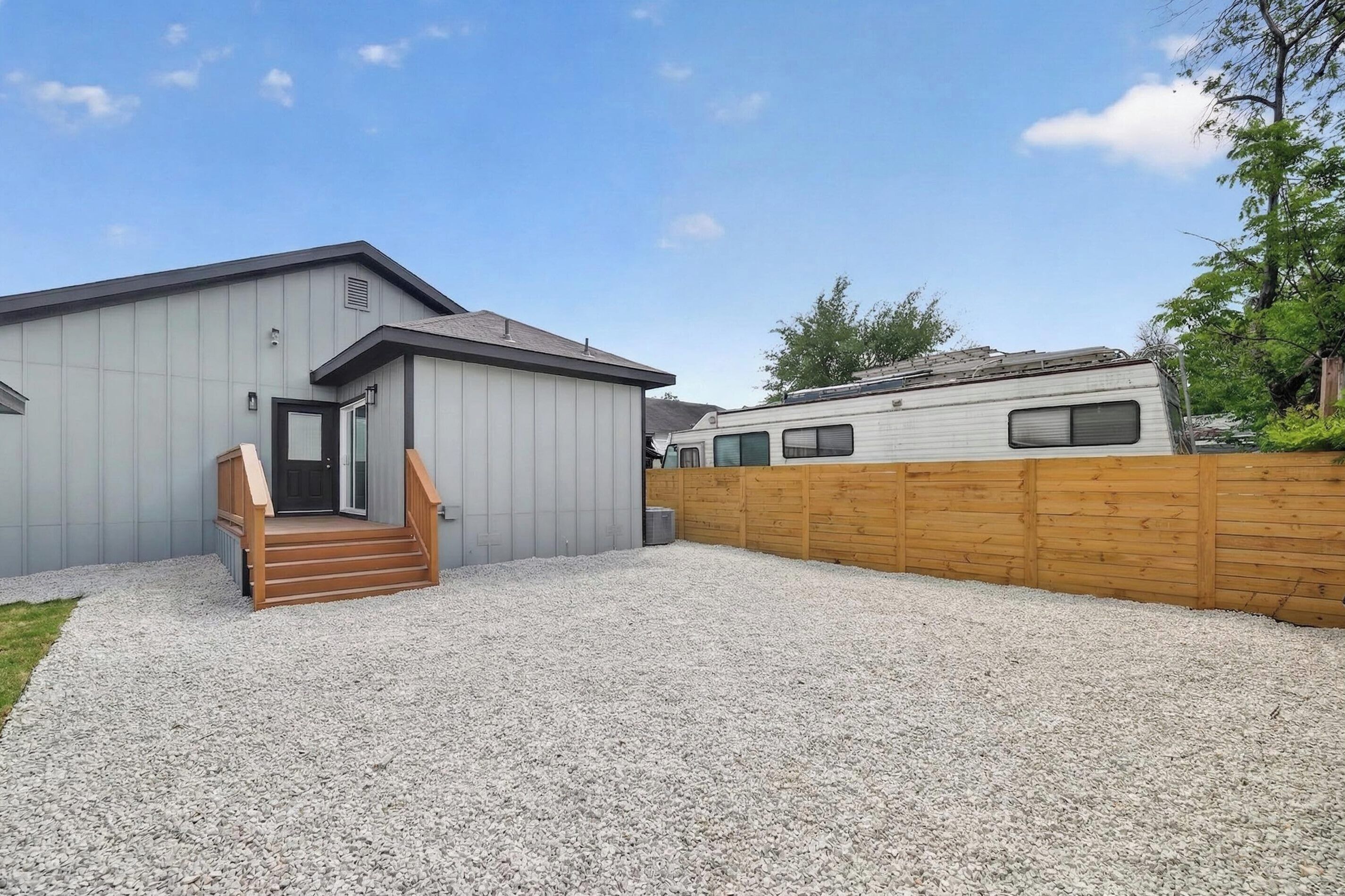 A modern building with a gravel driveway, wooden steps, and a wooden fence.