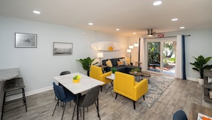 A modern living room with a dining area, a sofa set, and a view through a glass door to an outdoor space. - Relax at our fully renovated peaceful beach condo in Satellite Beach (Satellite Beach)