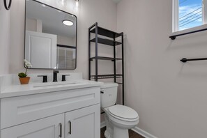 A bathroom with a white vanity, a toilet, a black metal shelf, and a window with a view of the sky. - Modern Studio  Luxury finishes Steps to Downtown (Columbus)