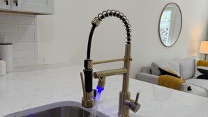 Een moderne keuken met een RVS spoelbak, een gouden kraan en een blauwe lichtaccent.