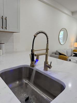 Eine moderne Küche mit Spüle aus Edelstahl, einem goldenen Wasserhahn und einer blauen Lichtleiste.