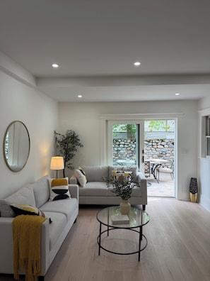 Ein Wohnzimmer mit einer Couch, einem Glastisch, einer Lampe und Blick auf eine Terrassenanlage.