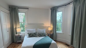 Een slaapkamer met een groot bed, twee nachtkastjes met lampen, een raam met gordijnen en een houten vloer.