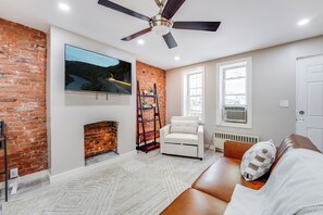 Ein Wohnzimmer mit Backsteinwand, Kamin, weißem Sofa, Deckenventilator und Wand-Fernseher.