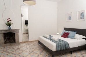 Un dormitorio con cama, chimenea, espejo y televisor instalado en la pared.