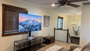 Una sala de estar con televisor, muebles de madera, ventilador de techo y cabeza de venado montada.
