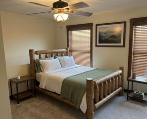 Un dormitorio con una cama de madera, un ventilador de techo y dos ventanas con persianas.