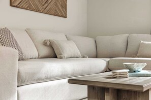 Een beige bank met een geweven plaid en een houten salontafel met boeken en een schaal.