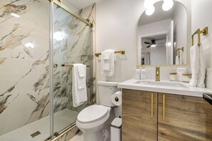 Een badkamer met een glazen douchecabine, een toilet, een wastafel met gouden details en een spiegel met een gouden lijst.