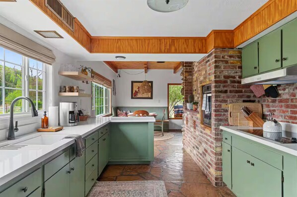 A kitchen with green cabinets, a brick wall, and a stone floor. - Vineyard Escape Near Sedona Shared Pool Hot Tub (Cornville)