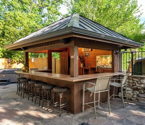 An outdoor bar with a wooden structure, bar stools, and a stone wall. - Vineyard Escape Near Sedona Shared Pool Hot Tub (Cornville)