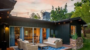 Uma casa moderna com um pátio, móveis de exterior e um pequeno galpão.